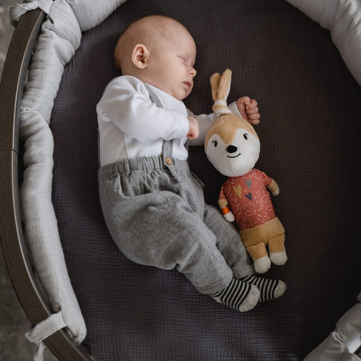 Schlafendes Baby im Babybett, daneben liegt die Spieluhr Ivy die Häsin