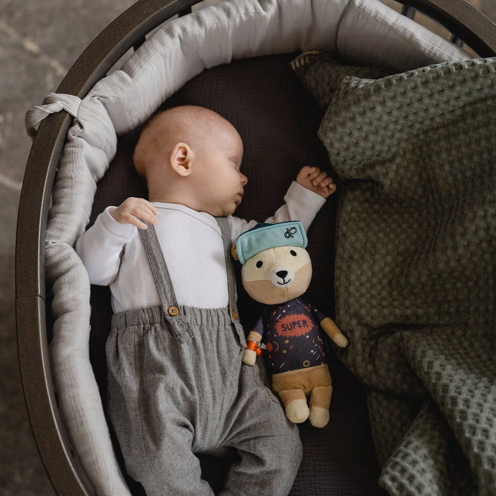 Schlafendes Baby im Babybett, daneben liegt die Spieluhr Jay der Bär