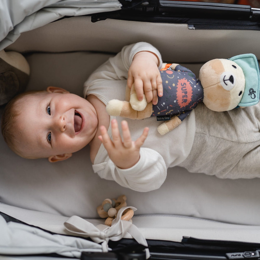 Lachendes Baby im Kinderwagen hält die Spieluhr Jay der Bär im Arm