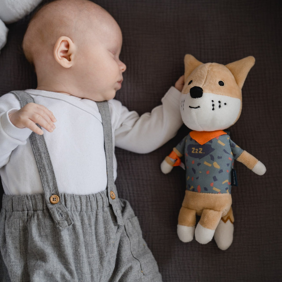Schlafendes Baby im Babybett, daneben liegt die Spieluhr Peter der Fuchs
