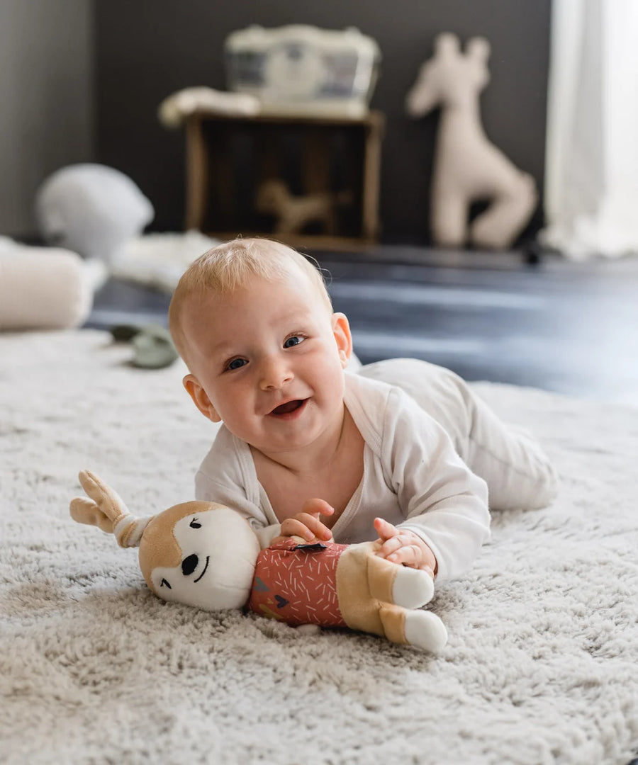 Baby liegt auf dem Teppich und lacht, Ivy die Häsin unter den Händen.