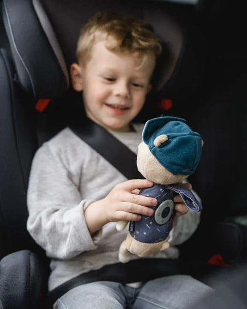 Junge im Kindersitz lacht und hält Jay den Bären in den Händen.
